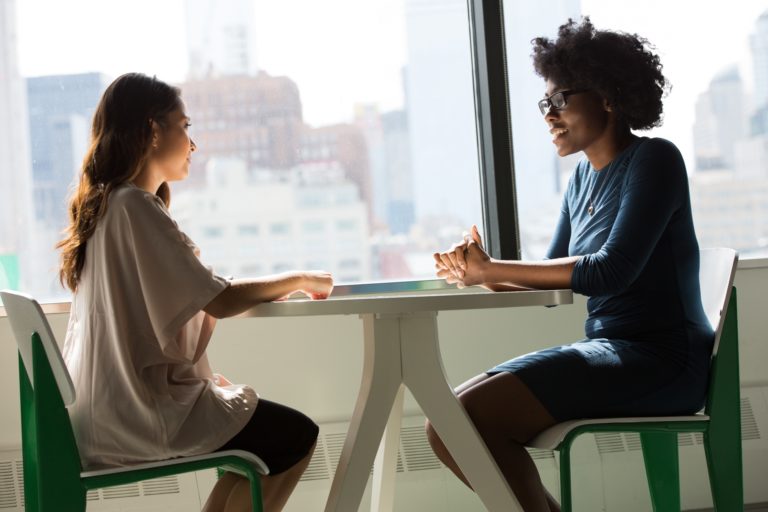 Deux femmes assises autour d'une table devant une baie vitrée, dans un contexte professionnel